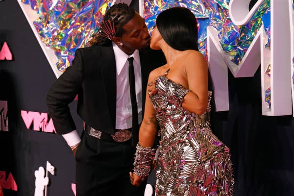 Offset and Cardi B sharing a kiss on the red carpet, one in a tailored tuxedo, the other in a strapless, metallic embellished gown