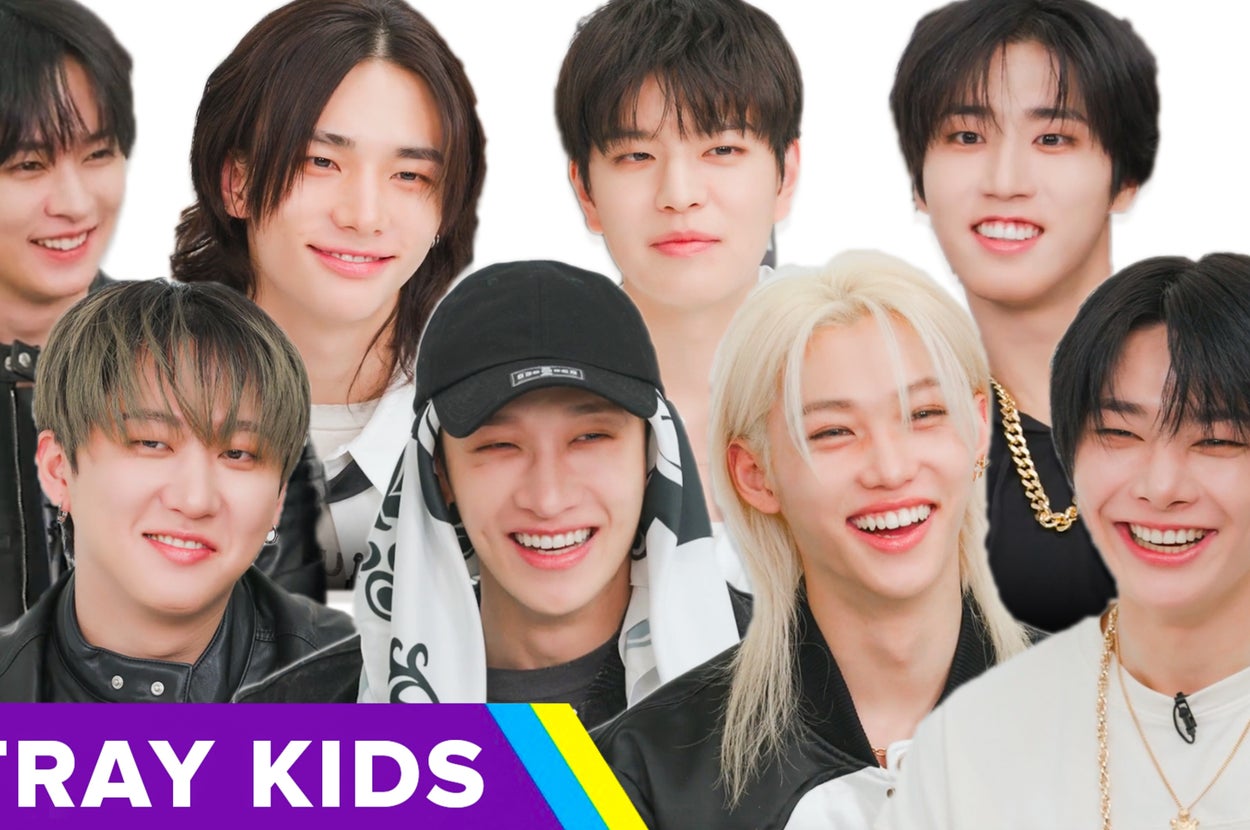Eight members of a music group, Stray Kids, smiling. Casual attire includes leather jackets, a black cap, and accessories