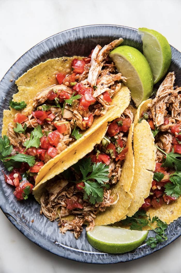 Three tacos filled with shredded chicken, pico de gallo, and cilantro on a plate with lime wedges