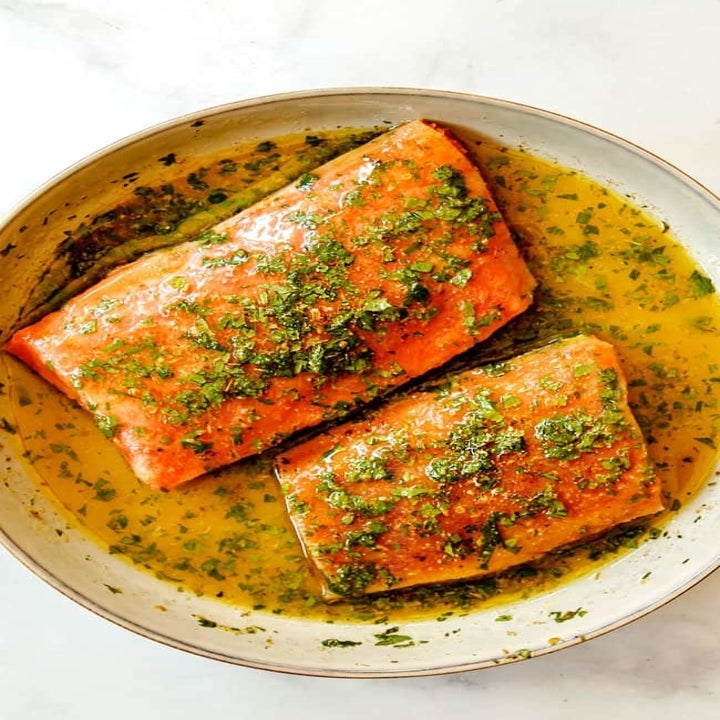 Two pieces of salmon fillets in a dish, covered with a garlic herb butter sauce