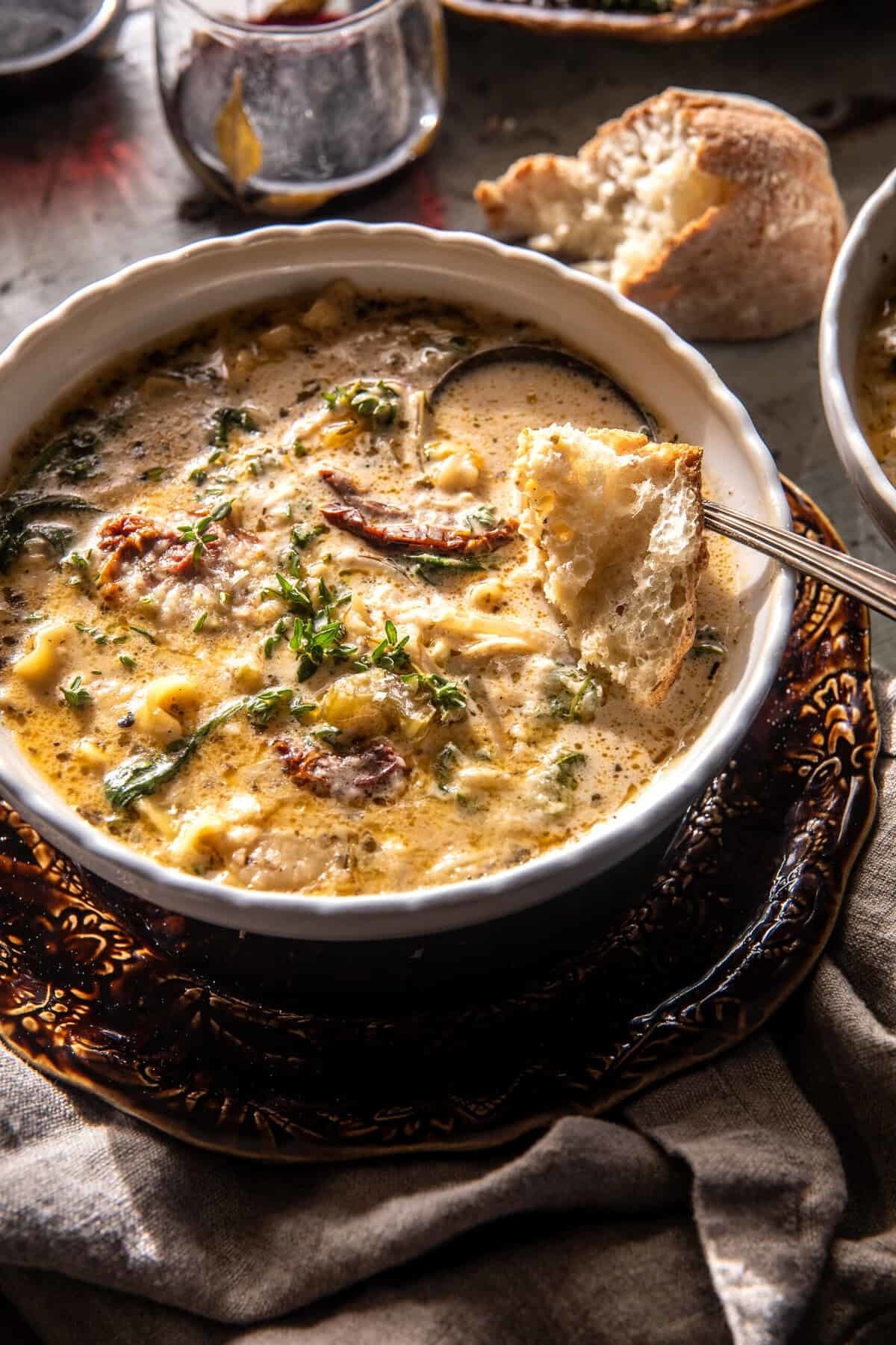 Creamy soup with herbs and tomatoes in a bowl, served with crusty bread on a plate