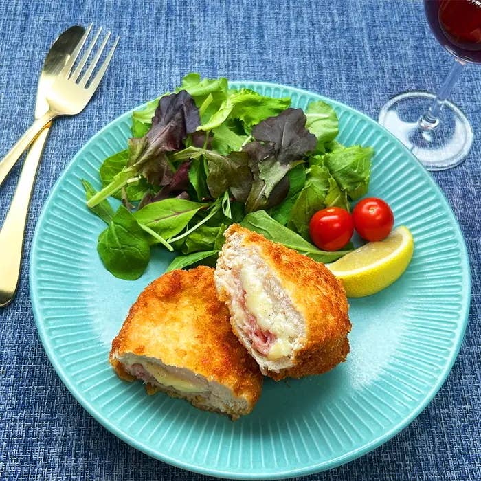 皿に盛られたコルドンブルー、サラダ、チェリートマト、レモンが置かれた食事の様子。