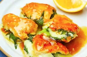 料理の写真：ハーブと溶けたチーズを使ったチキン料理が皿に盛られ、レモンが添えられている。