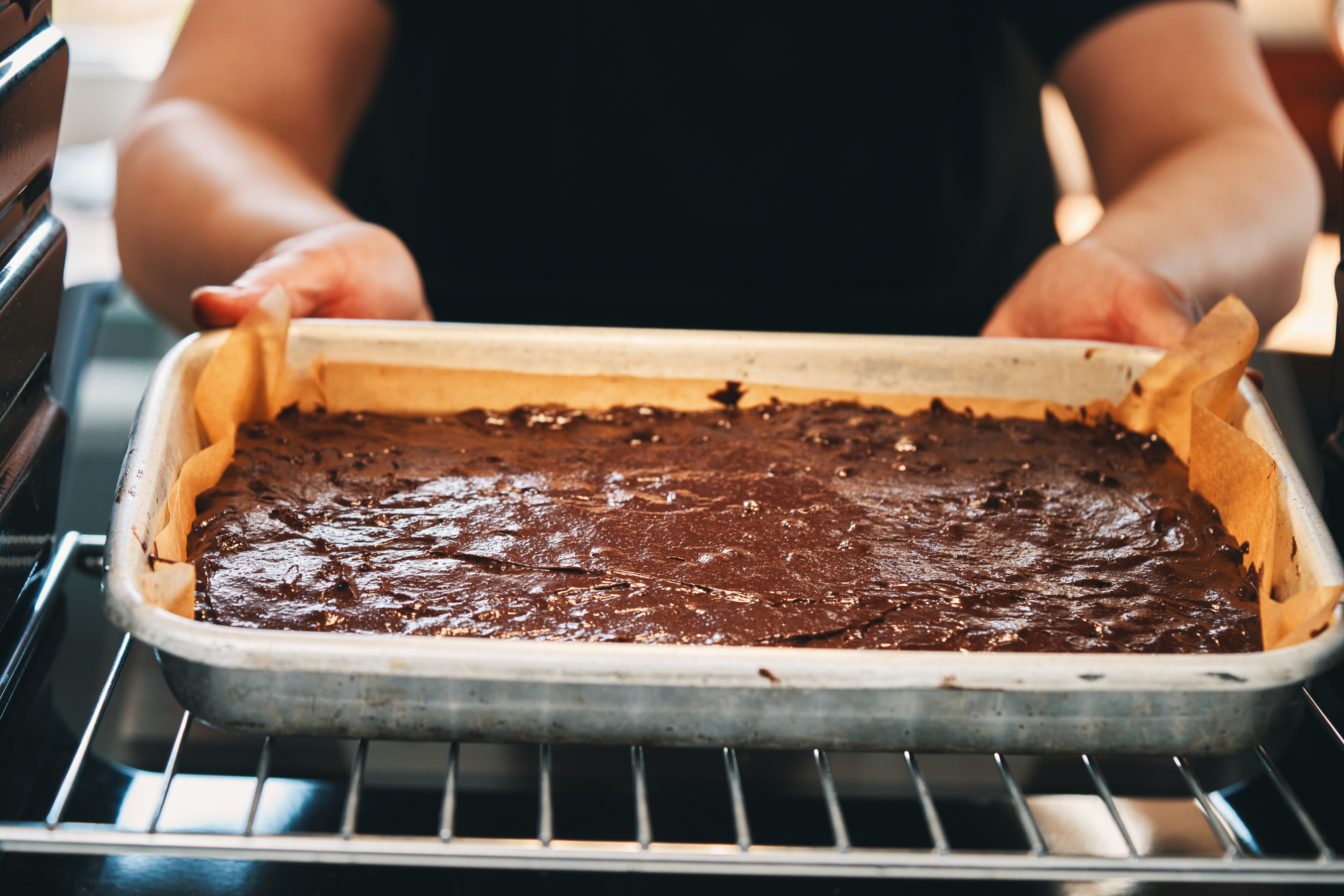 Person placing a tray of chocolate brownie batter into an oven