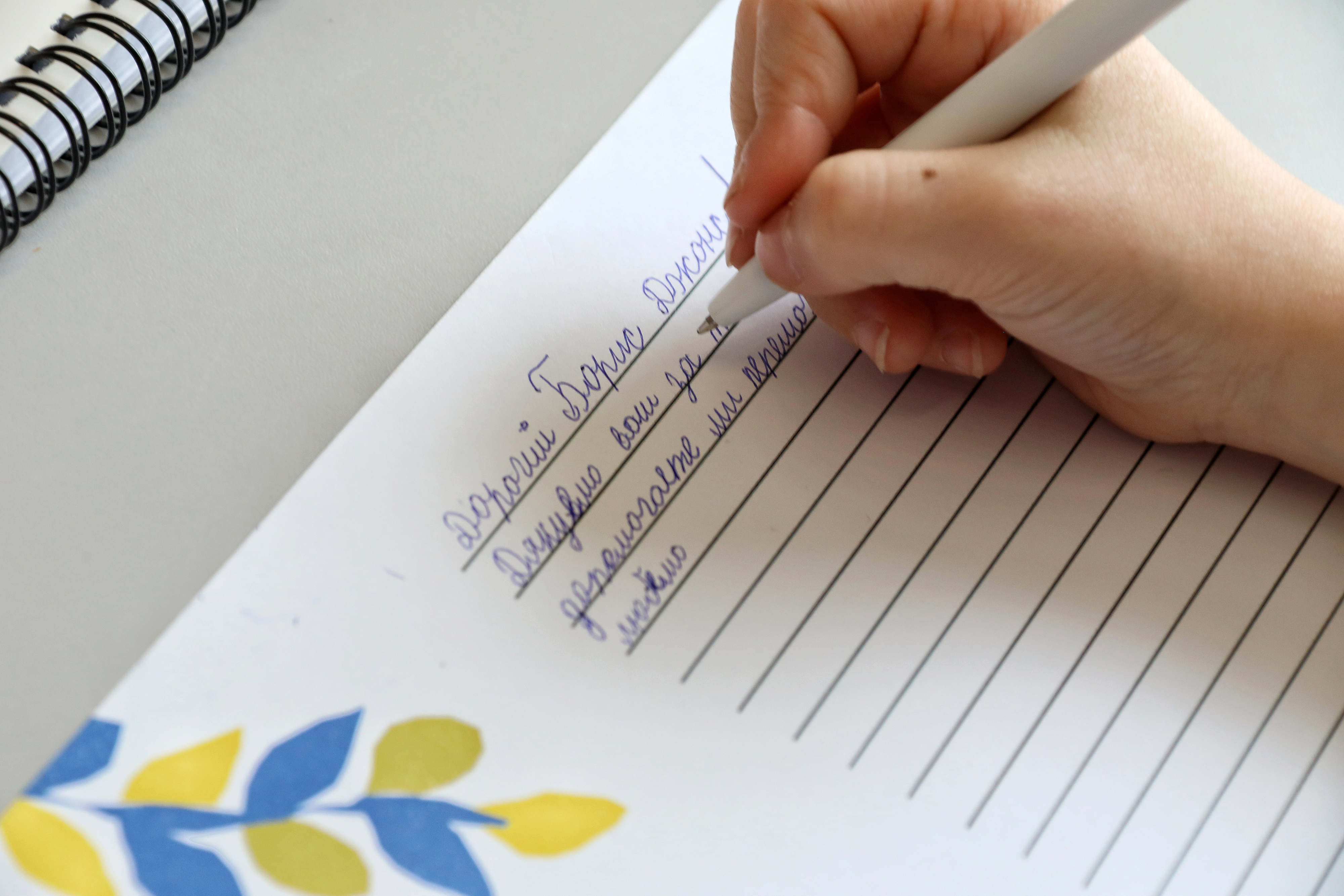 A hand writing in cursive on lined paper with floral decoration at the bottom left