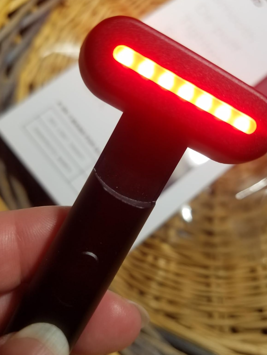 Person holding an LED facial tool with glowing lights, positioned over a woven surface