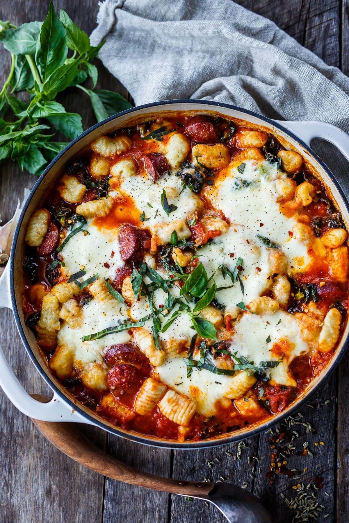 Baked gnocchi with melted cheese, tomato sauce, and fresh basil in a pan on a wooden table