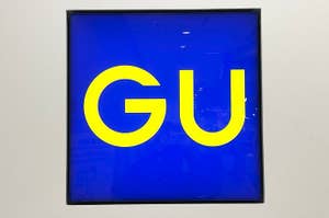 Illuminated store sign with the letters "GU" in yellow on a bright background