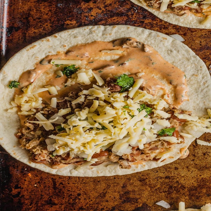 Tortilla topped with beans, cheese, and a creamy sauce, garnished with cilantro on a baking sheet