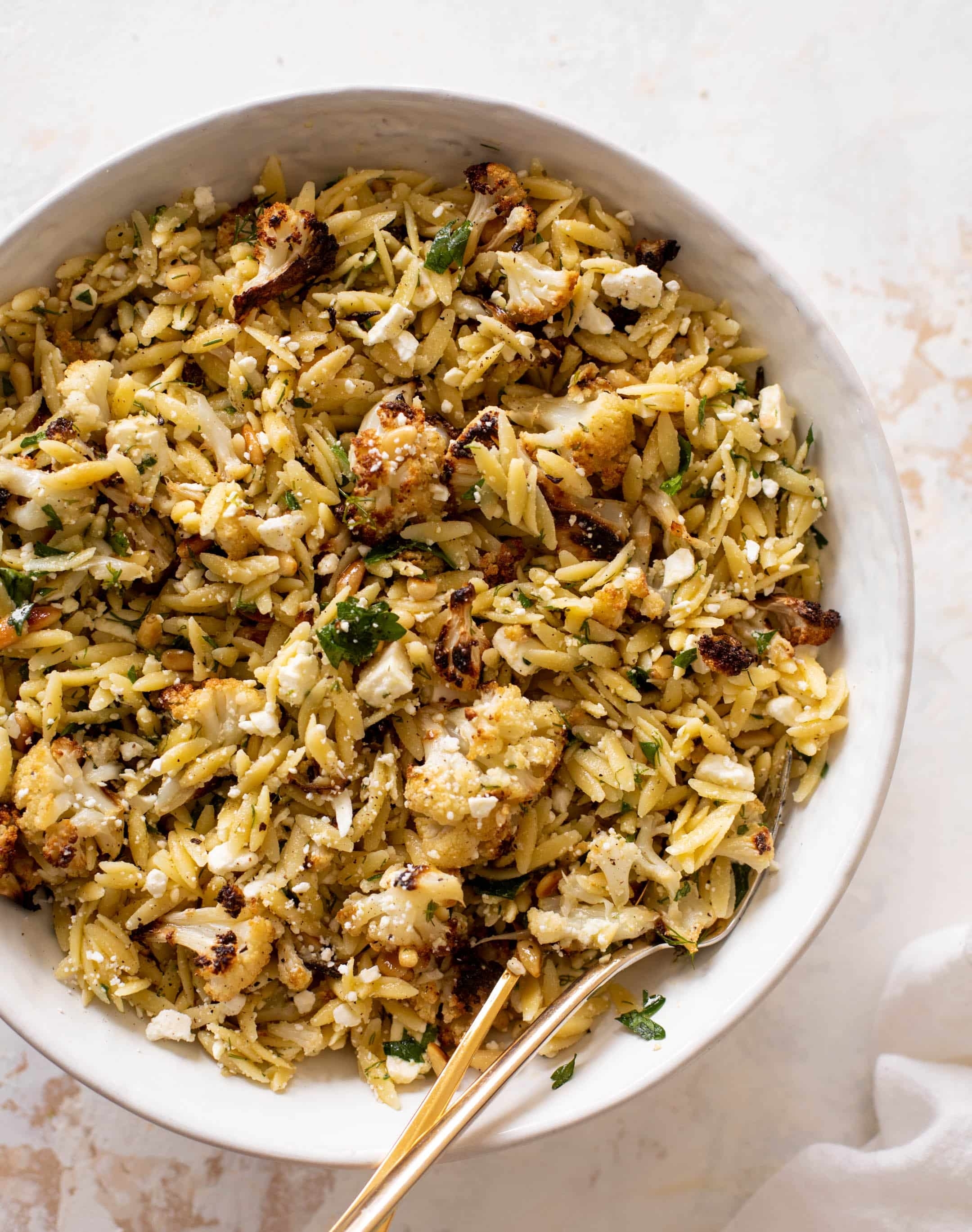 Bowl of orzo salad with roasted cauliflower, herbs, and crumbled cheese, served with a fork