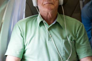 男性が飛行機の座席でヘッドホンを着けてリラックスしている。