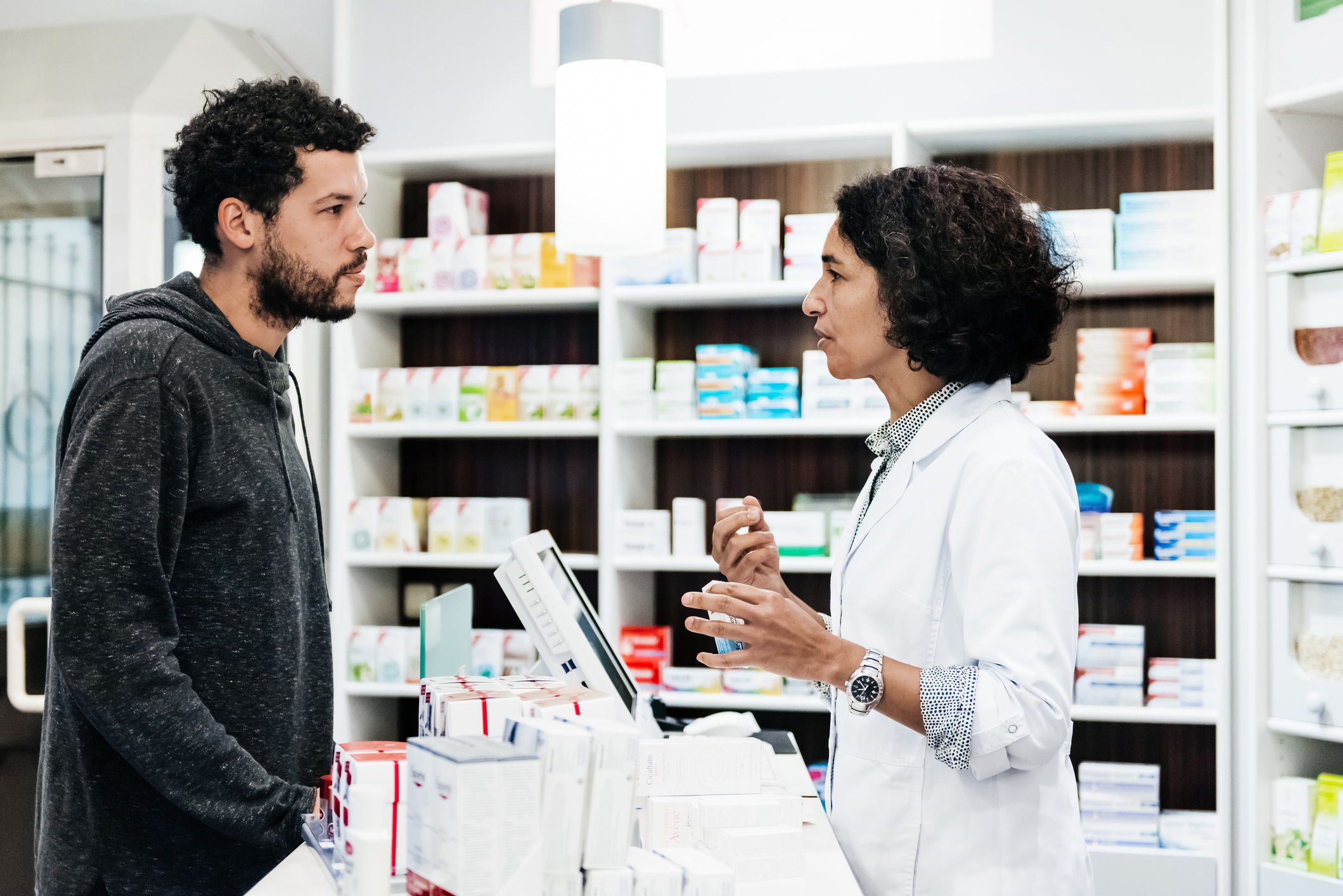 Pharmacist in a white coat discusses medication with a customer in a pharmacy setting