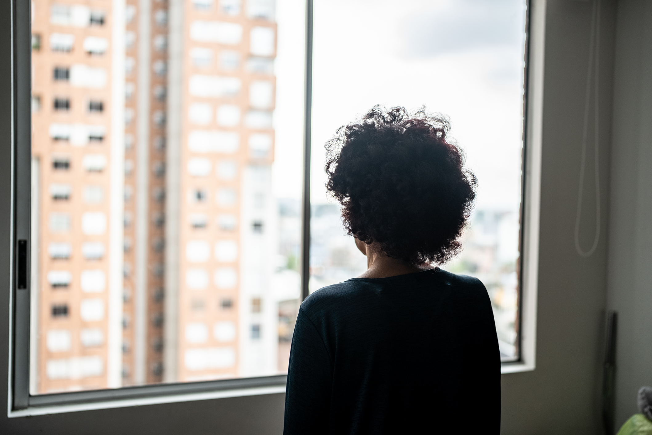 Person with curly hair looks out a window at tall city buildings, conveying contemplation or focus on work-life balance