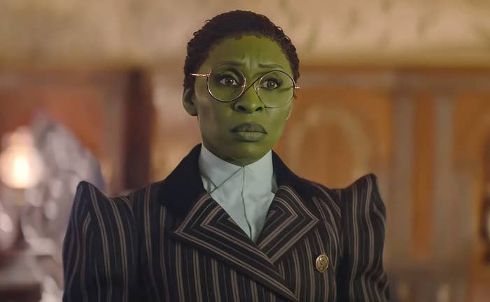 Cynthia Erivo wearing a pinstripe suit and glasses, with green makeup, in an elegant setting