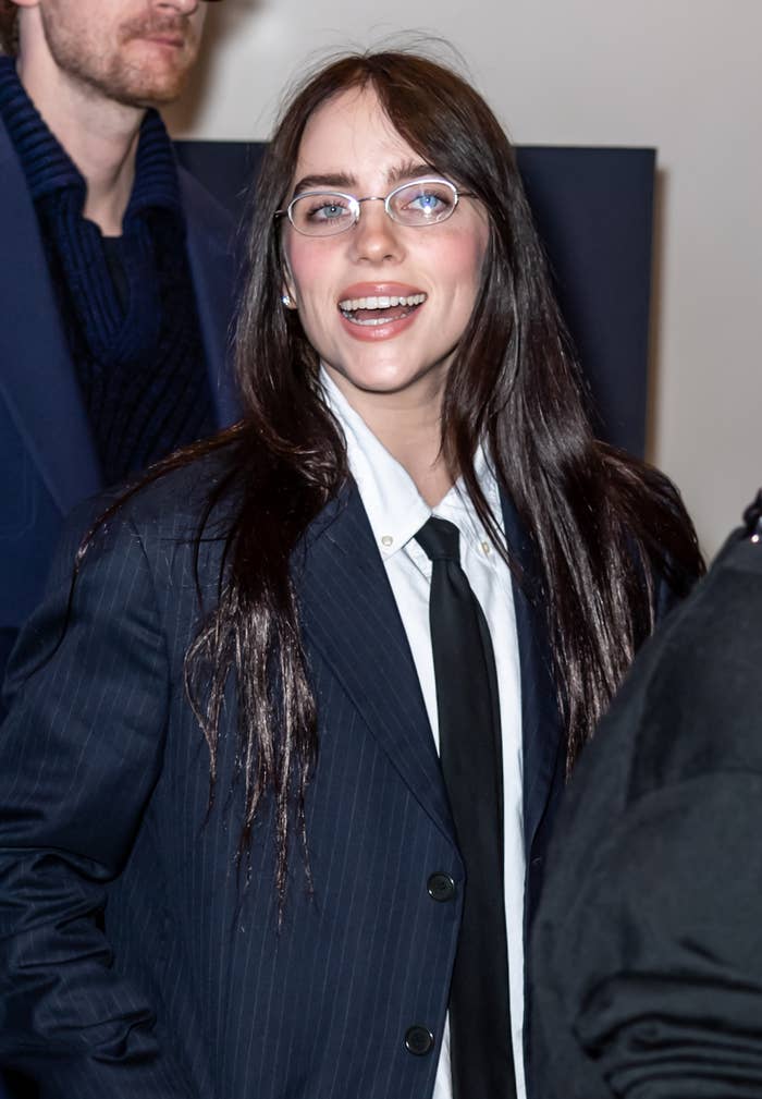 Person in a suit and tie with long hair and glasses, smiling at an event