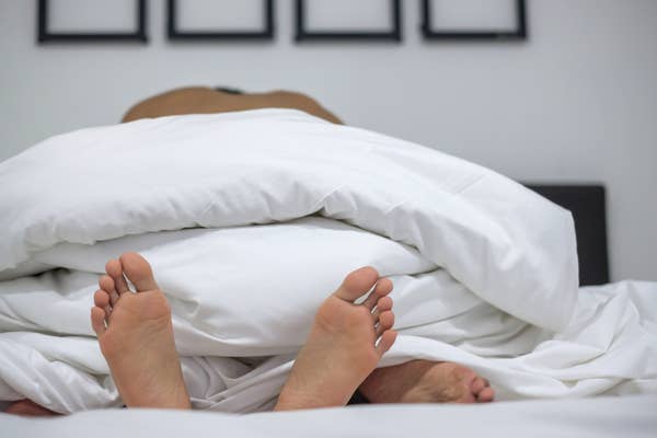Two pairs of feet peek out from under white bed covers, suggesting intimacy and relaxation