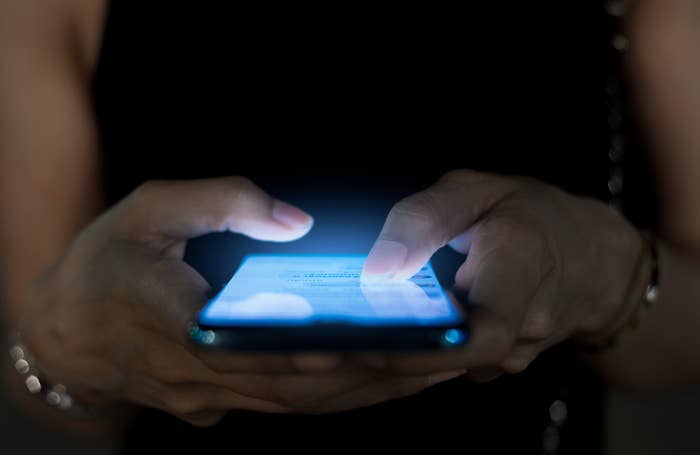 Person texting on a smartphone in a dark setting, fingers tapping the screen, with light illuminating their hands
