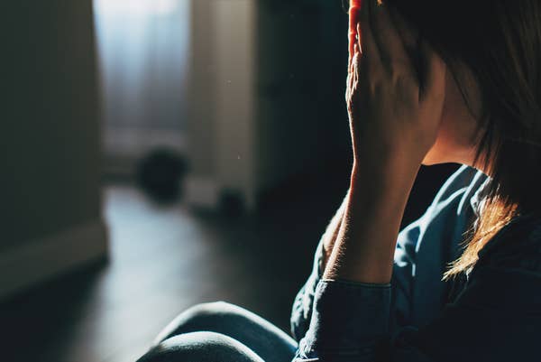 Person sitting on the floor with hands covering their face, in a dimly lit room, conveying a sense of emotional distress or contemplation