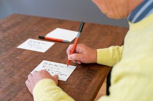 男性が机で手紙を書いている。机の上にもう一枚の紙と数本のペンが置かれている。