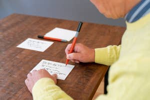 男性が机で手紙を書いている。机の上にもう一枚の紙と数本のペンが置かれている。