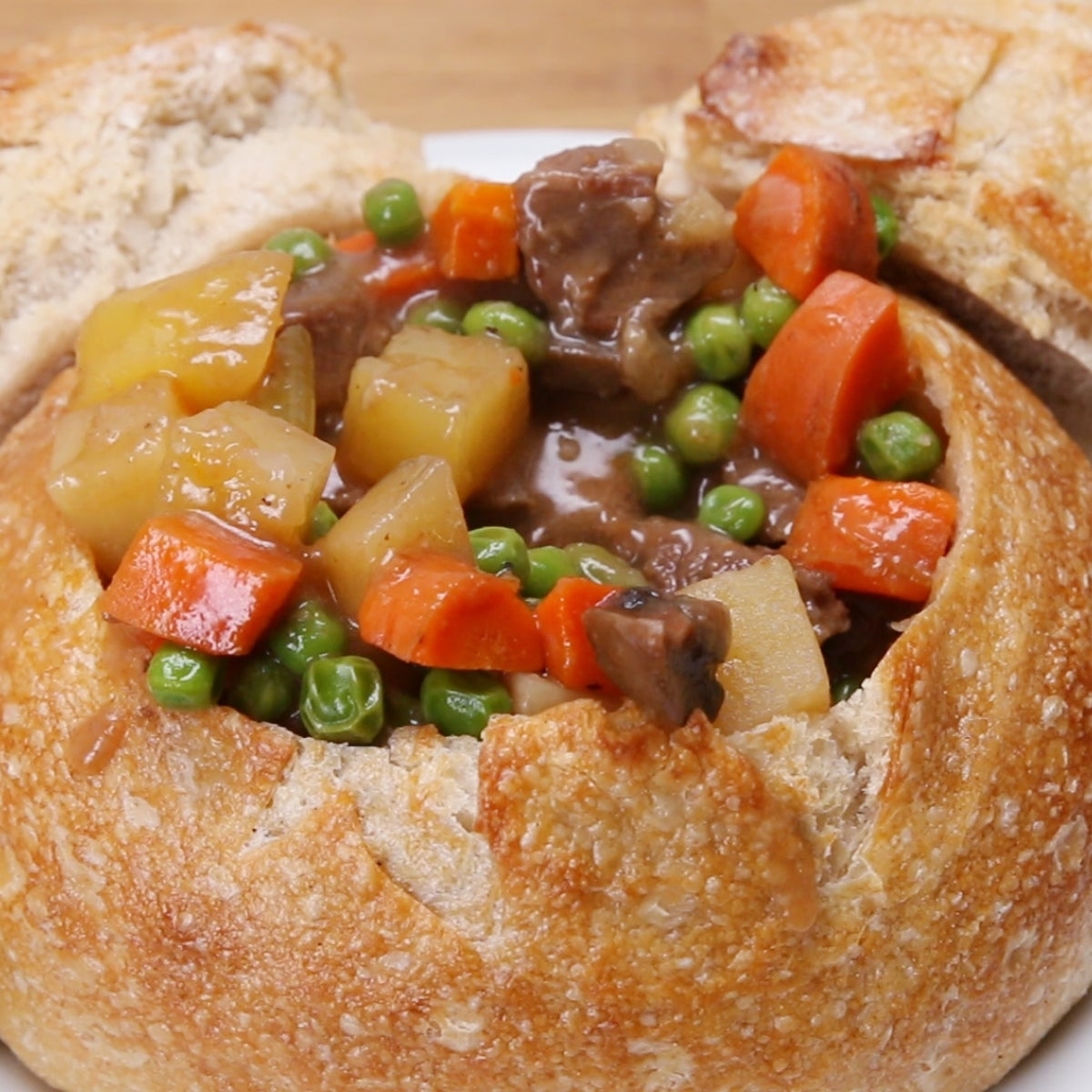 Hearty vegetable and beef stew served in a round bread bowl, featuring carrots, peas, and potatoes