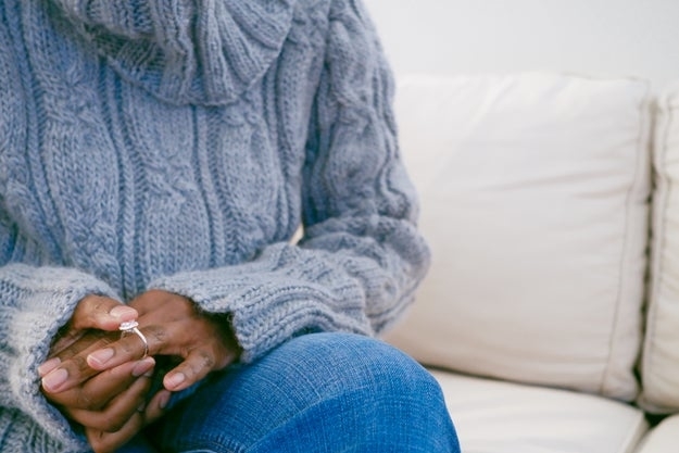 Person sitting on a couch wearing a chunky knit sweater and jeans, holding a ring