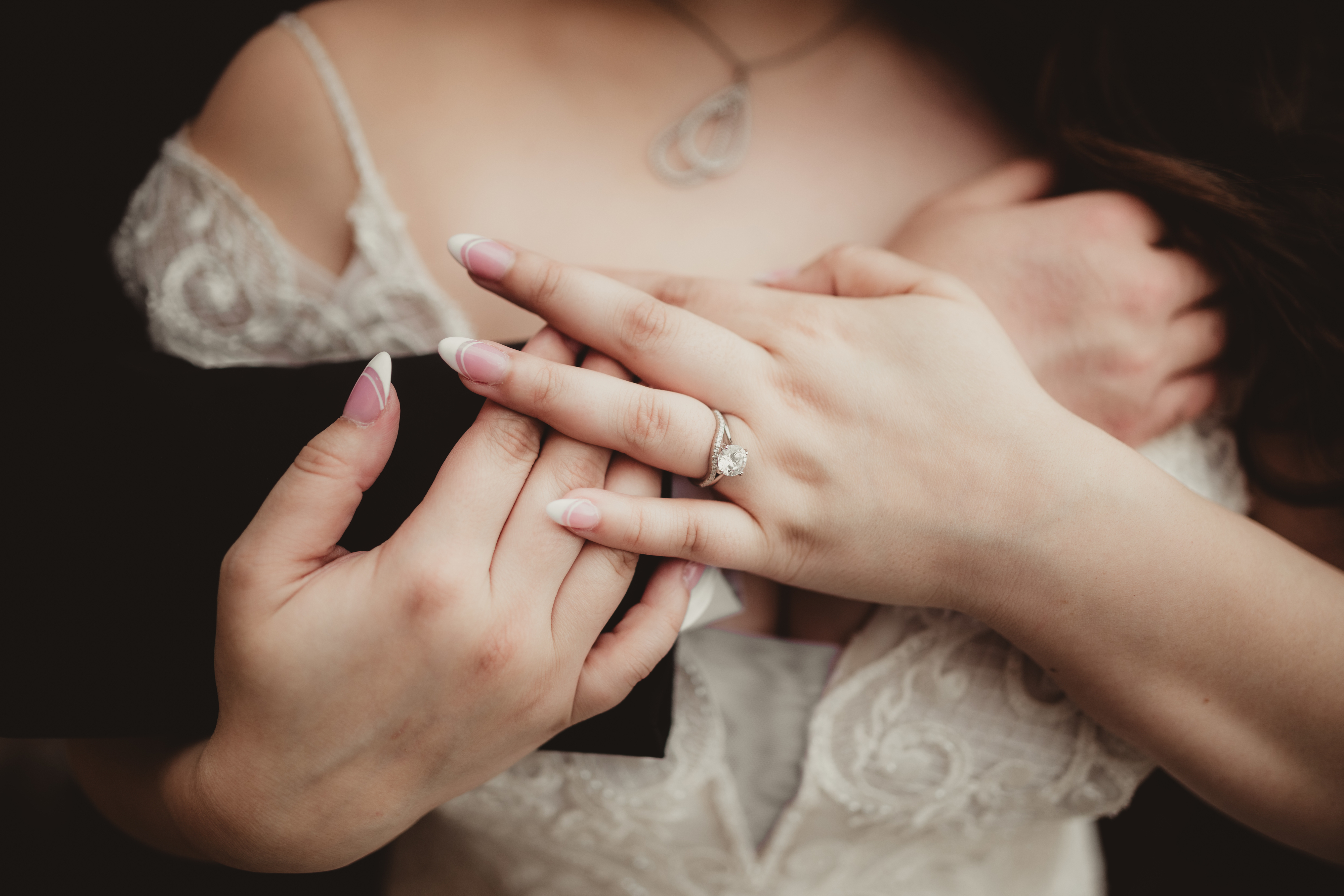 Close-up of hands clasped, featuring an engagement ring. Person wears lace patterned clothing