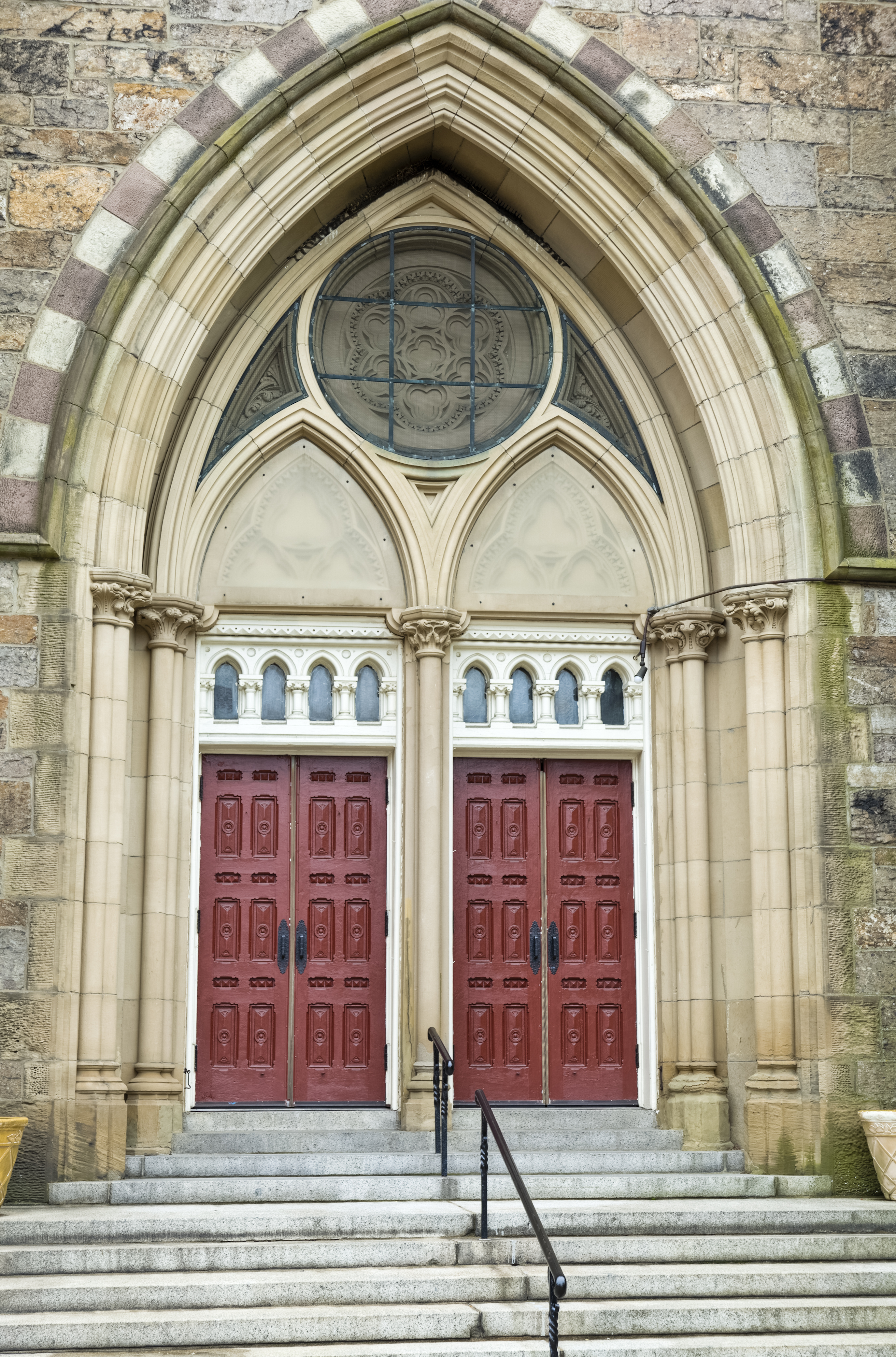 Gothic-style church entrance with ornate stonework and two large wooden doors. Steps and railing lead up