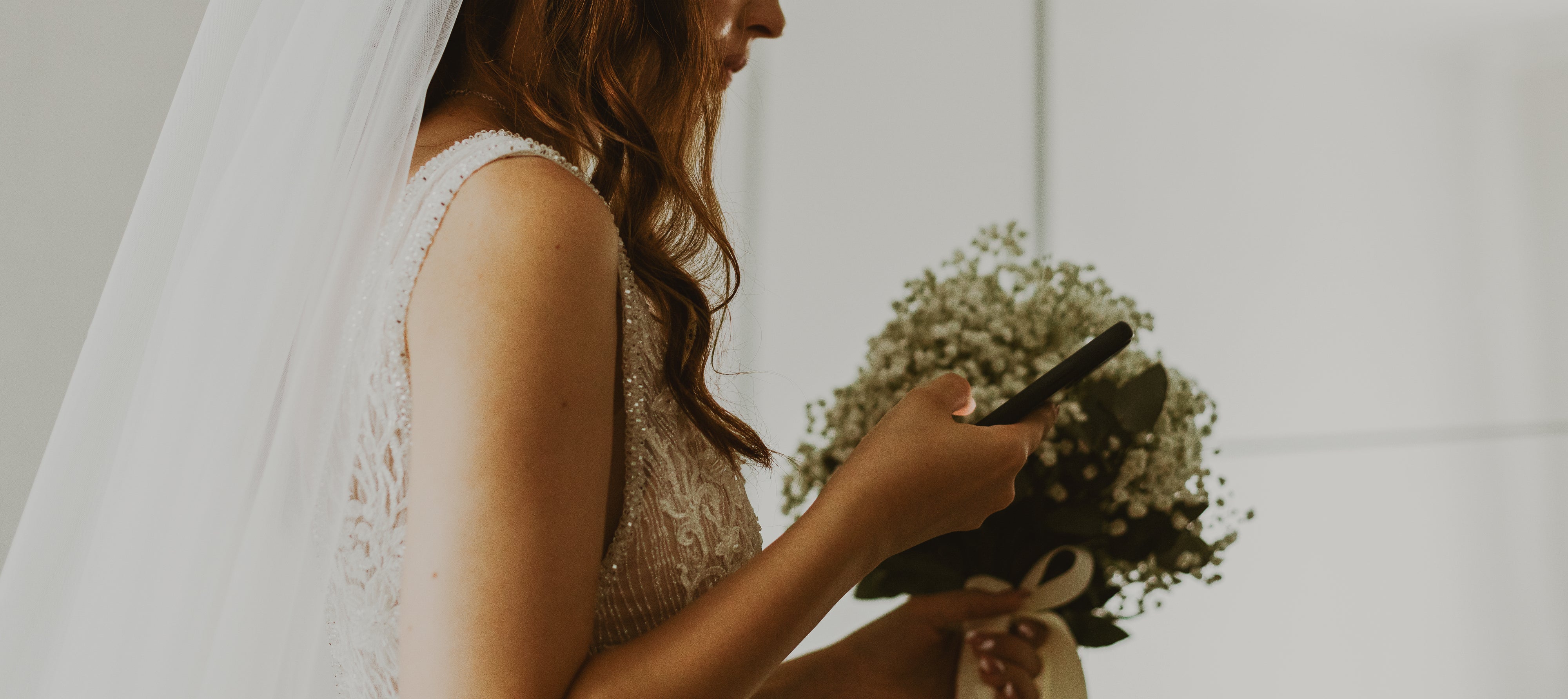 Bride in a lace dress holding a bouquet, looking at her phone