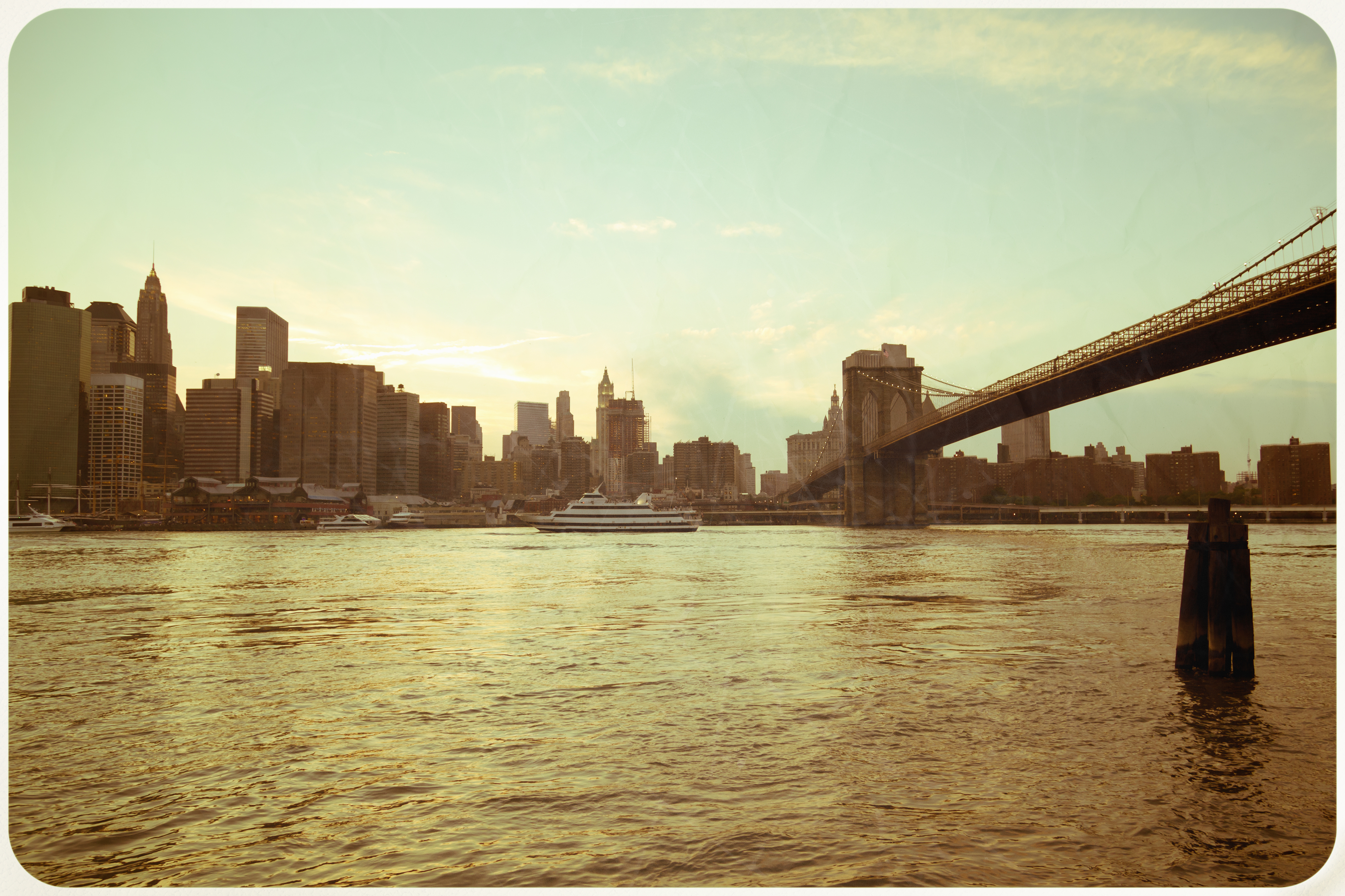 City skyline with a bridge over water at sunset, featuring skyscrapers and a docked yacht on the calm river