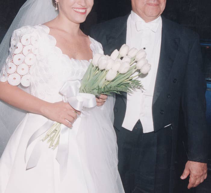 Bride in an elegant white gown with floral details, holding white tulips, stands beside a man in formal attire
