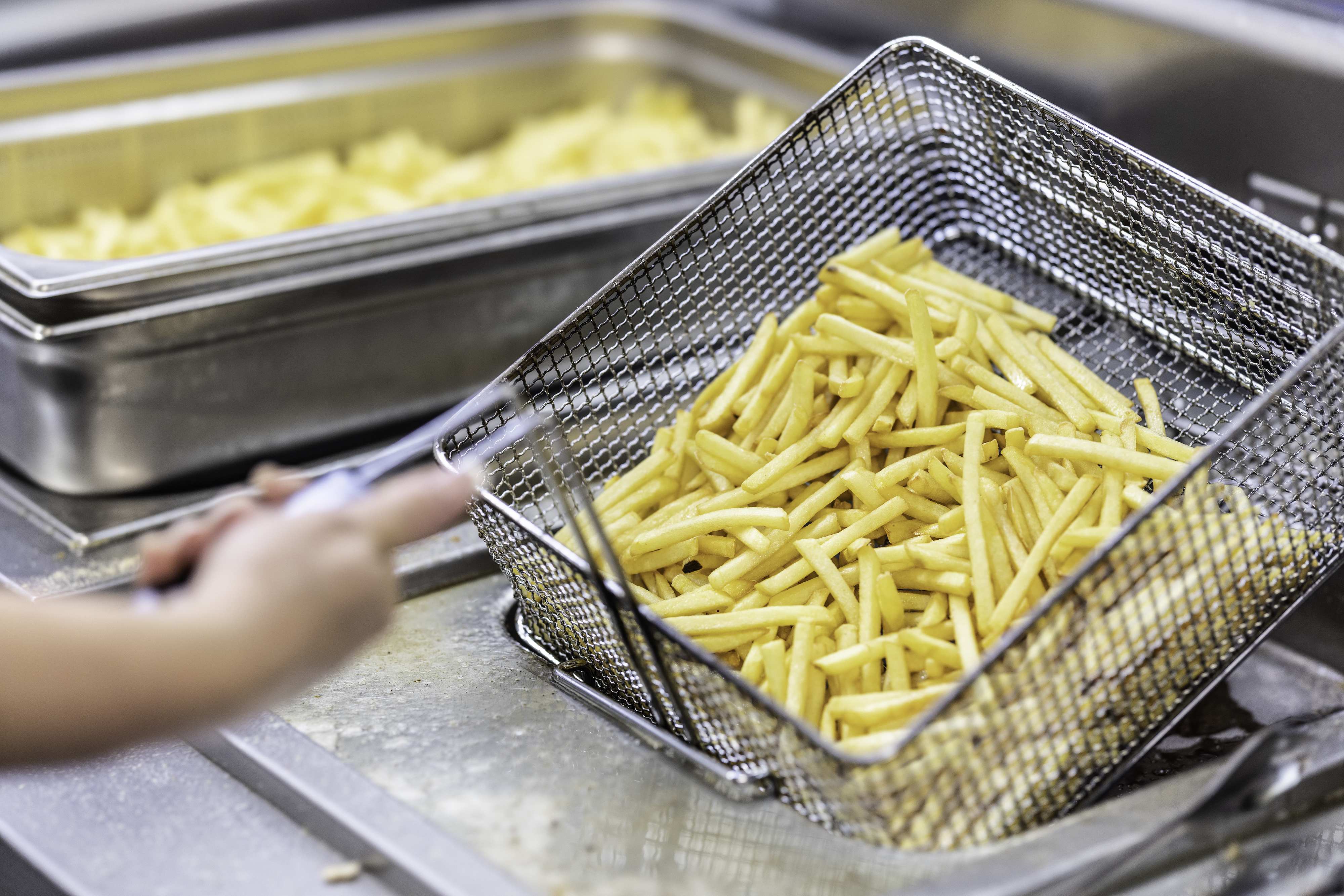 Person lifting basket of freshly fried French fries from fryer in a kitchen setting