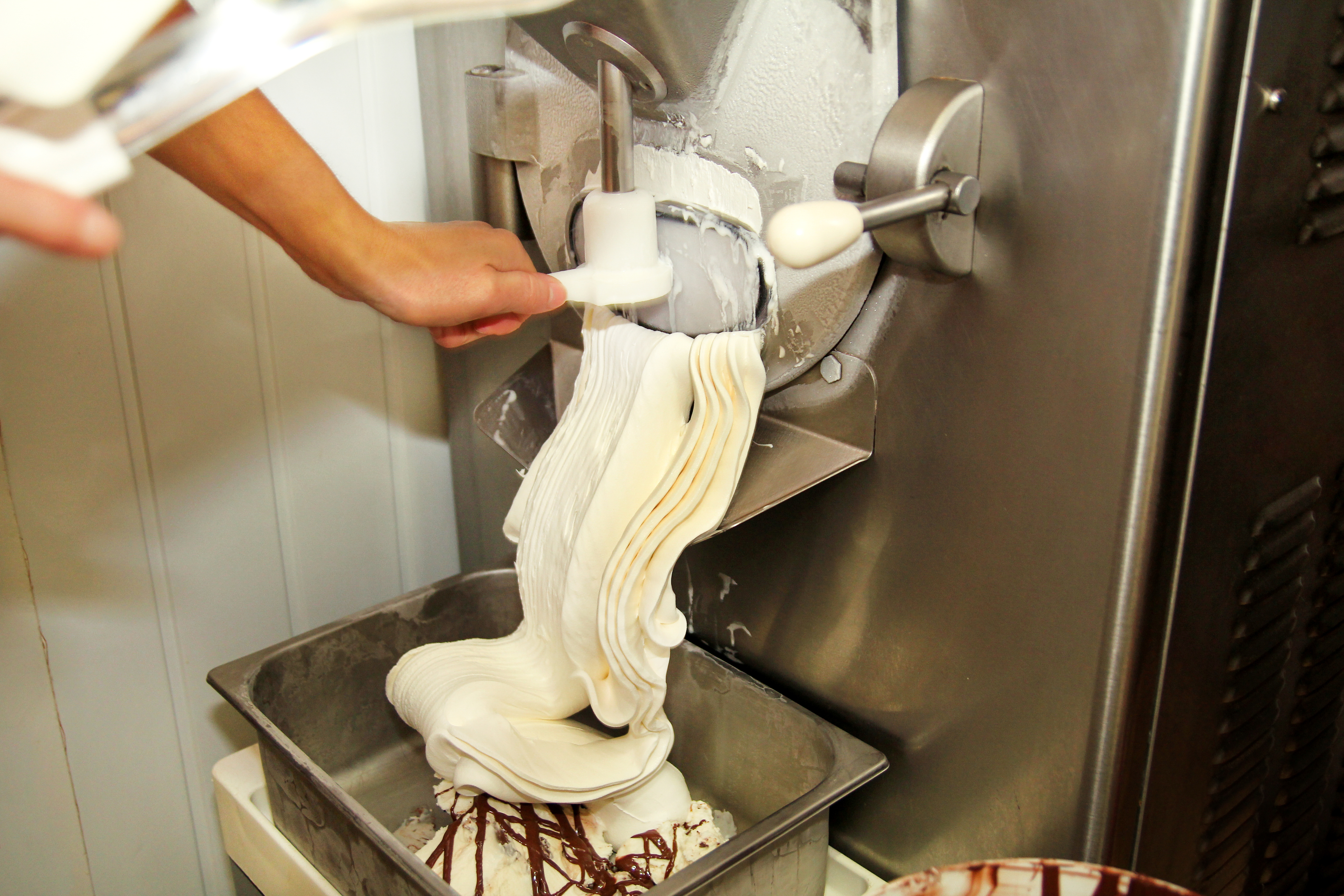 Ice cream being churned and extruded from a machine into a metal container