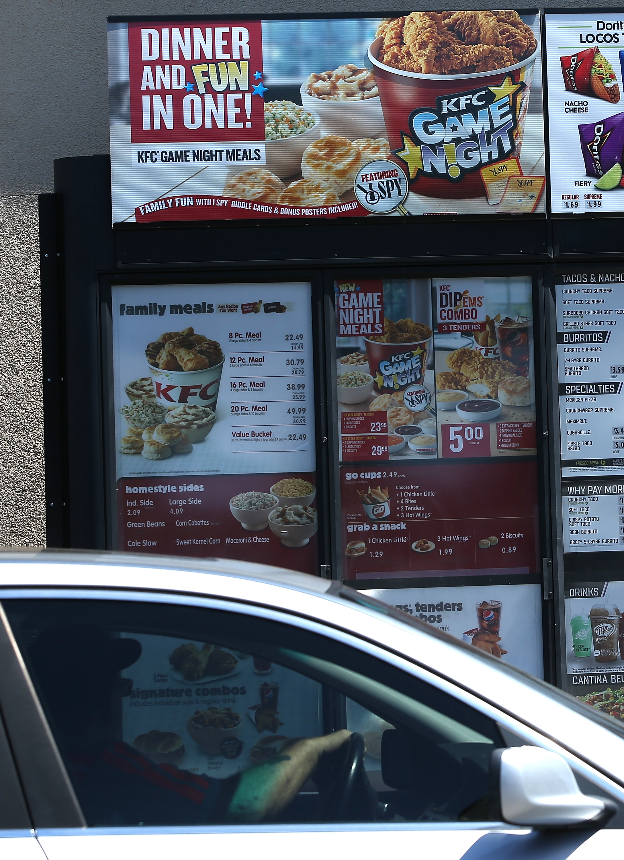 Drive-thru menu at KFC showing family meals, sides, and game night promotions. Price details visible but not clearly readable from car window