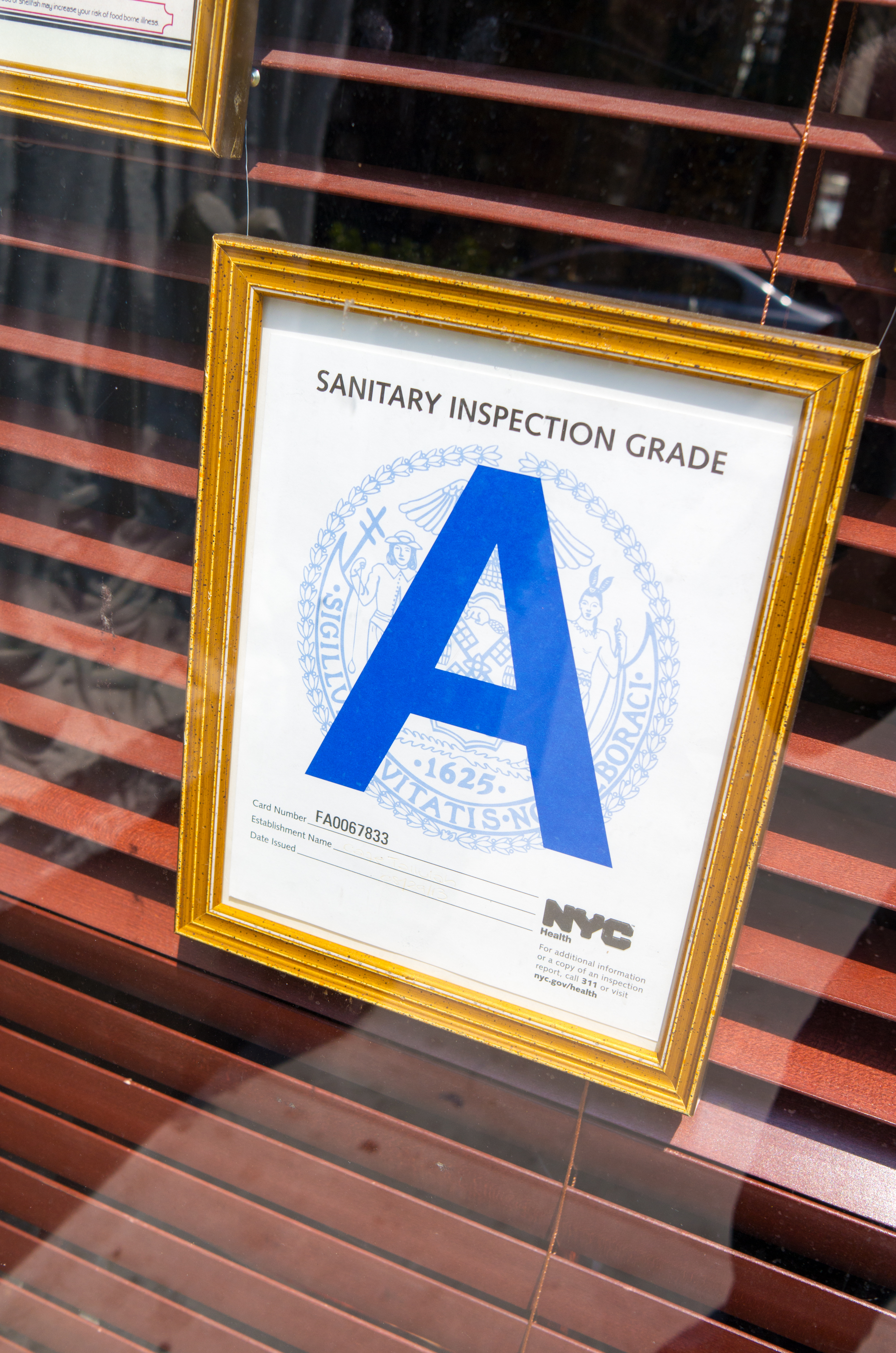 NYC sanitary inspection grade &#x27;A&#x27; certificate displayed in a gold frame on a window