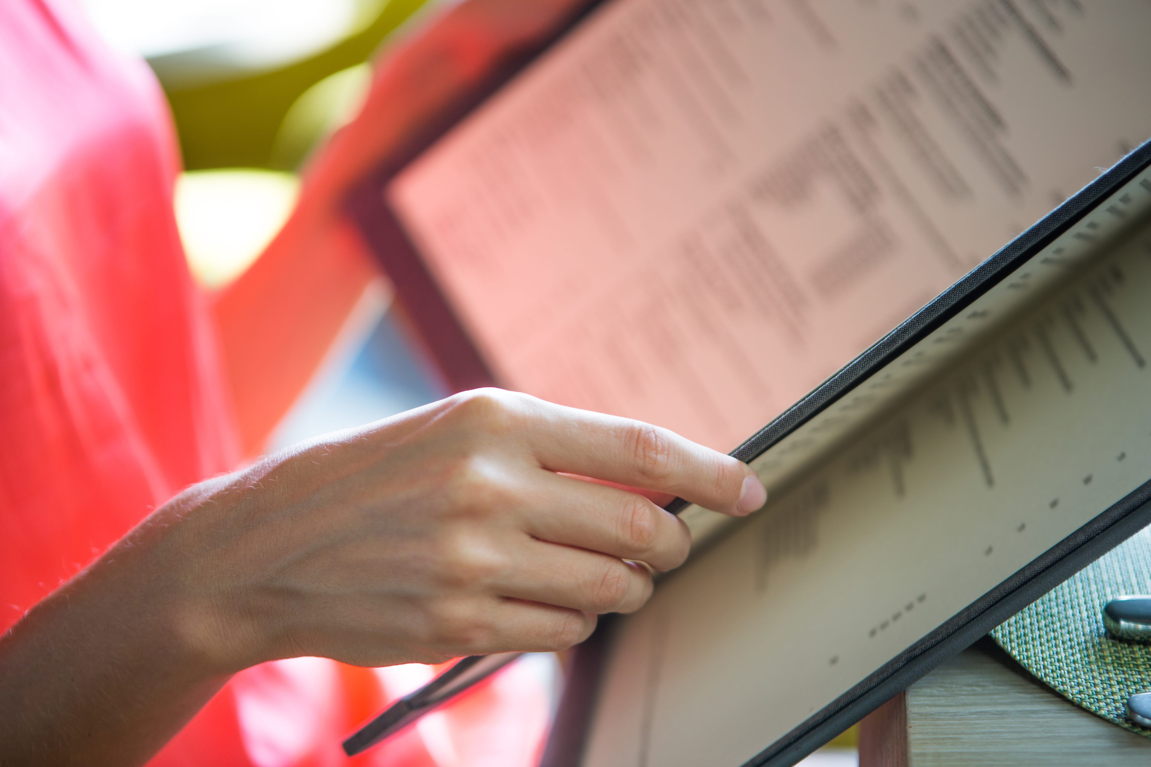 A person holding and reading a menu at a restaurant, focusing on their hand and part of the menu