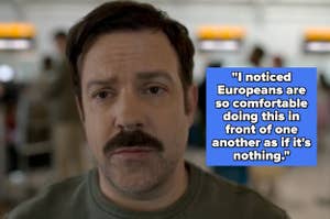 Person with a mustache and short hair standing in a busy airport setting, appearing thoughtful