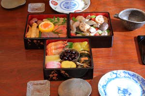 和食の重箱で、美しい盛り付けの料理を楽しむ人。伝統的な和室の場面。