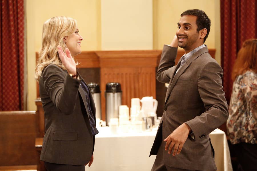 Two people in suits exchange a high-five in an indoor setting with a table and coffee setup in the background