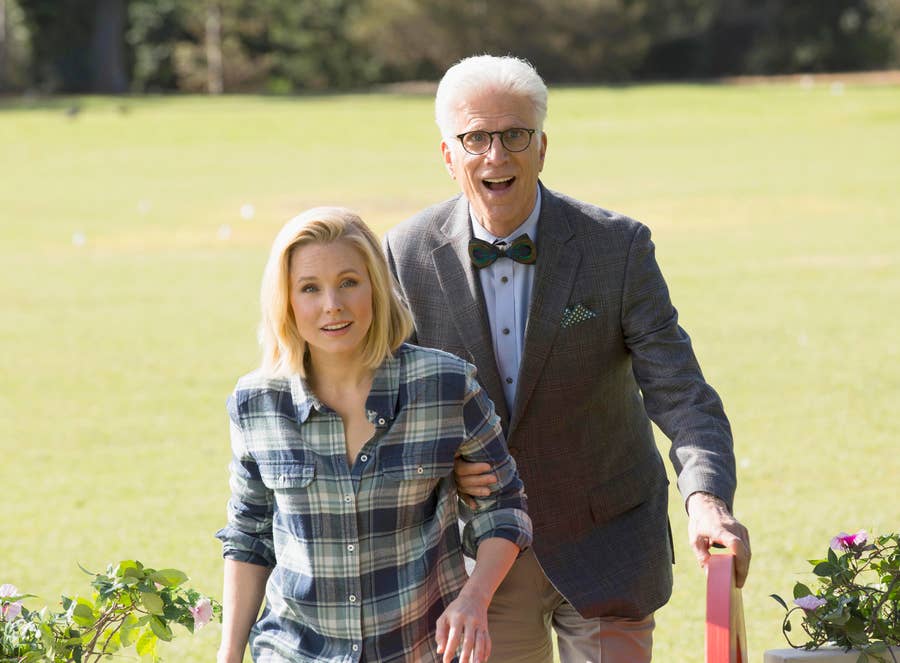 Two people walking outdoors, one wearing a plaid shirt and the other in a bow tie and suit. They appear surprised and are in a garden setting