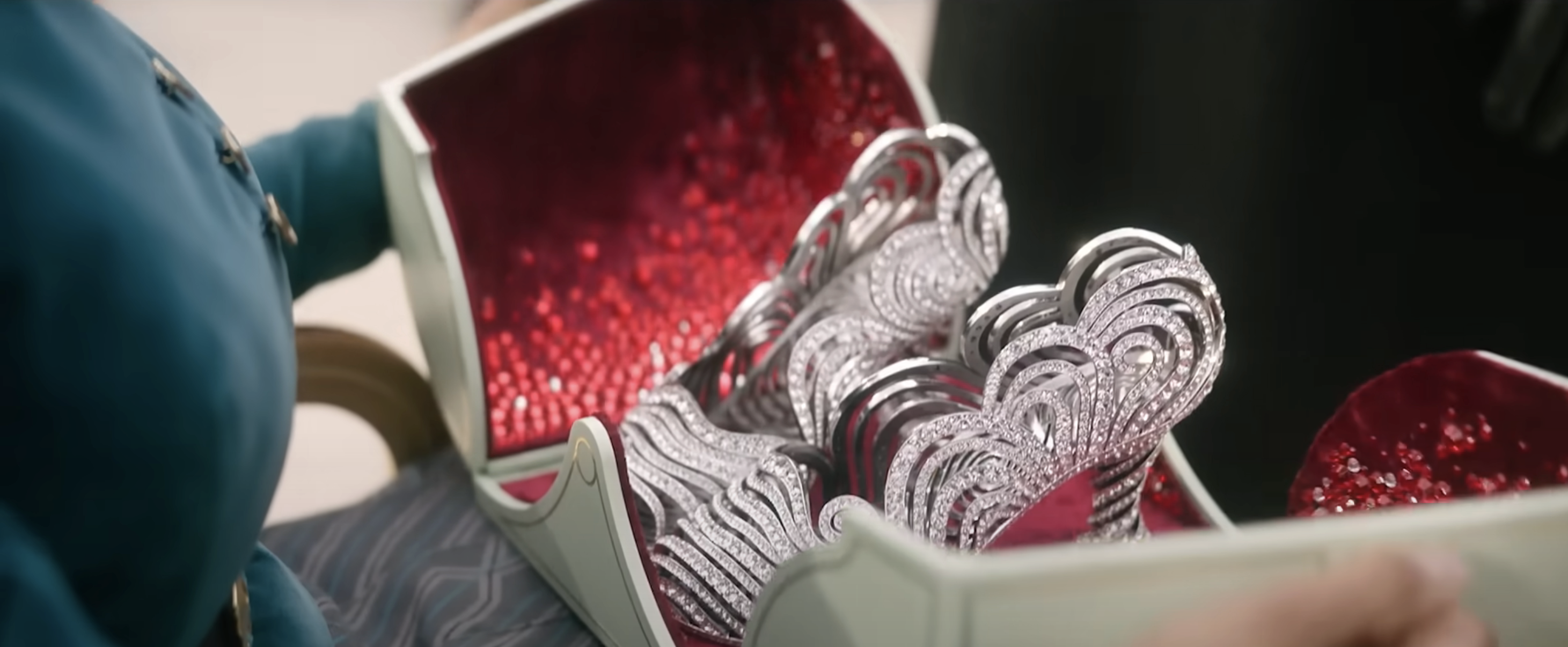 Nessarose holds an open case with sparkling, elaborate shoes inside, lined with shiny material