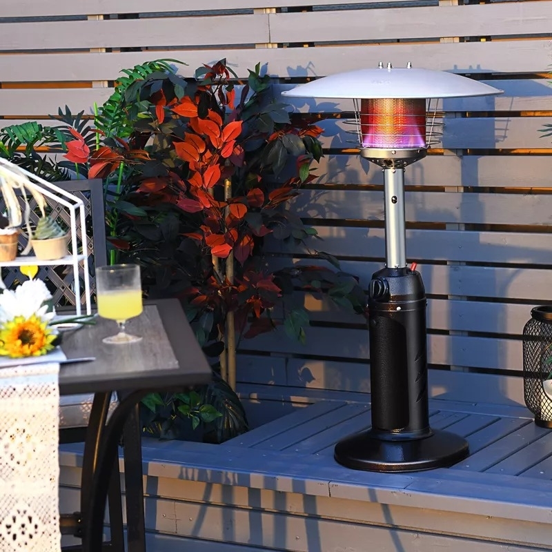 Outdoor patio area with a tabletop heater on a wooden bench, surrounded by plants and a table set for dining