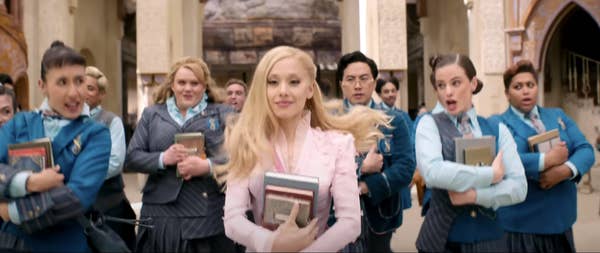 People in school uniforms holding books, walking in formation behind Glinda