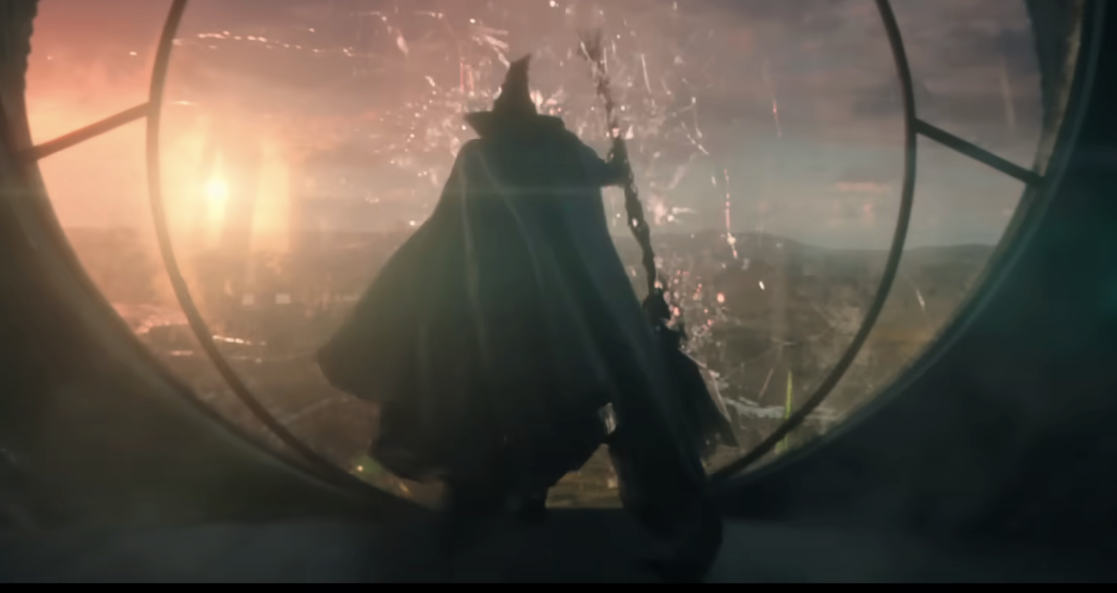 Elphaba, in a cape and hat holding a broom, jumps out a broken window