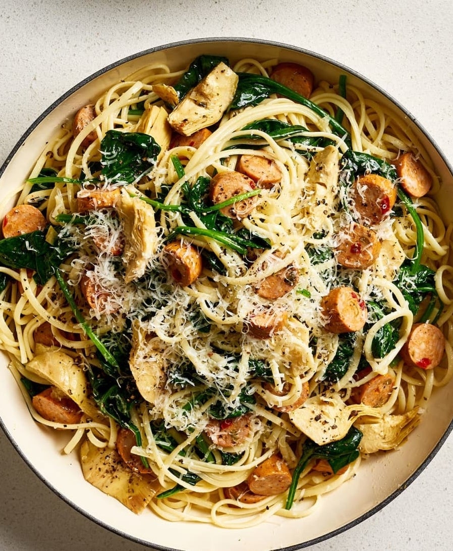 A pot of spaghetti with chicken, sausage, spinach, and grated cheese on top