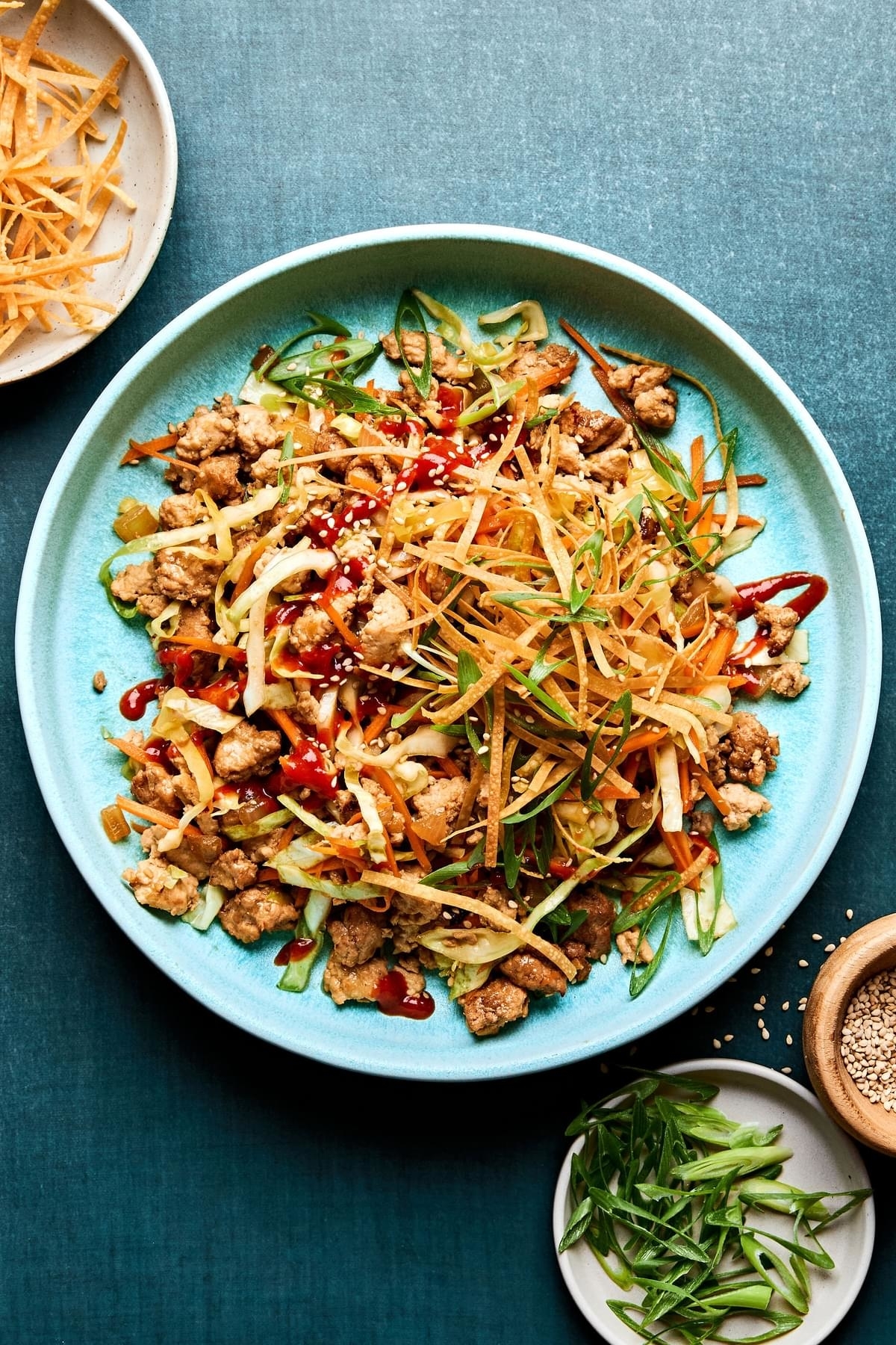 Stir-fried dish with ground meat, shredded vegetables, and sauce on a blue plate, garnished with sesame seeds and green onions