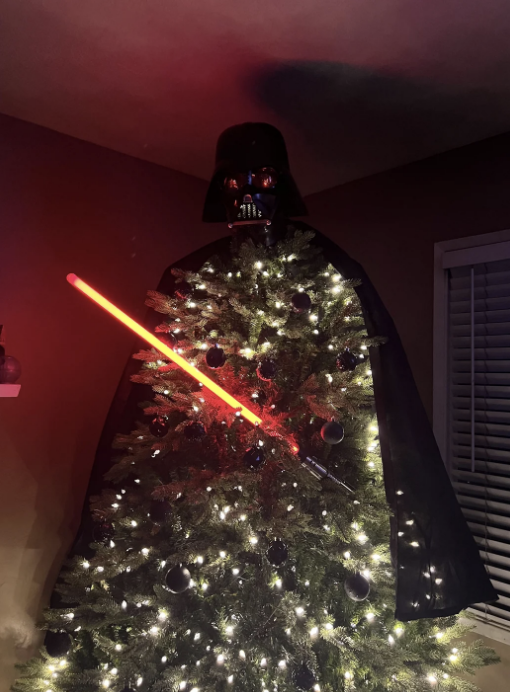 Christmas tree decorated with Darth Vader mask, cape, and a red lightsaber, resembling the Star Wars character