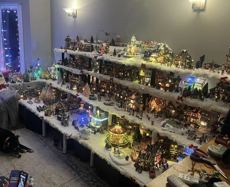 Holiday-themed miniature village display with lights, featuring various buildings, snowy rooftops, and a central carousel