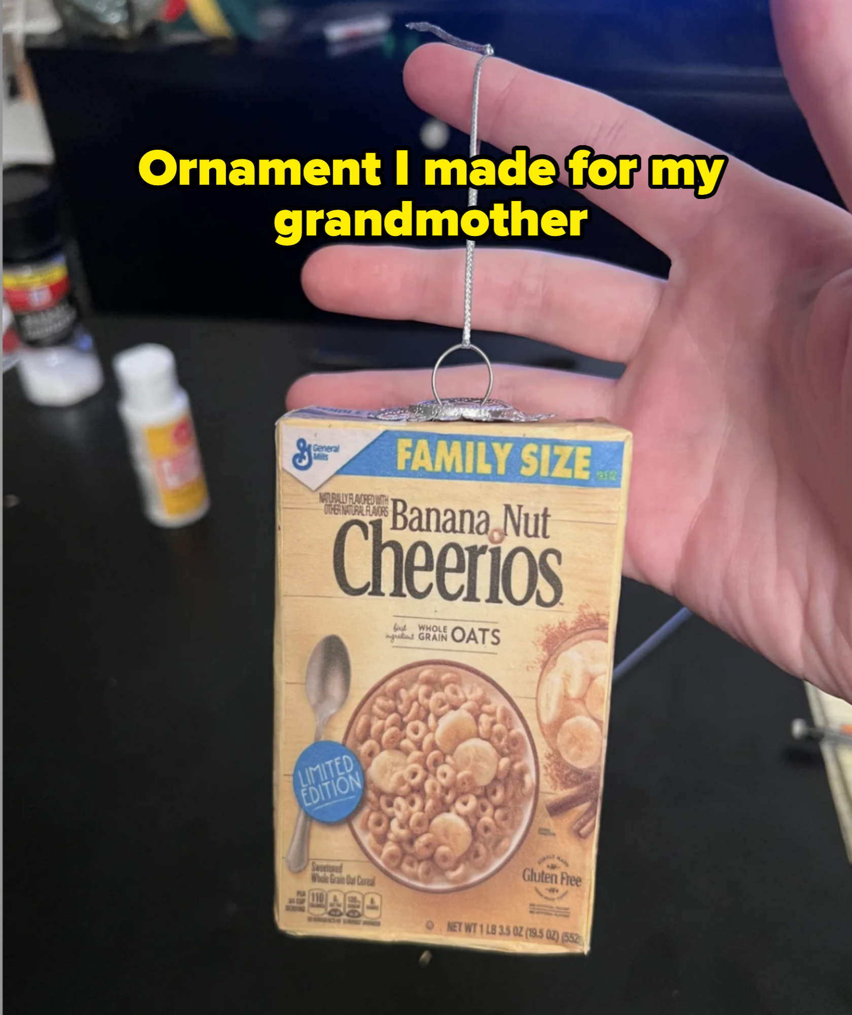 Hand holding a small, detailed model or ornament of a Banana Nut Cheerios cereal box labeled &quot;limited edition.&quot;