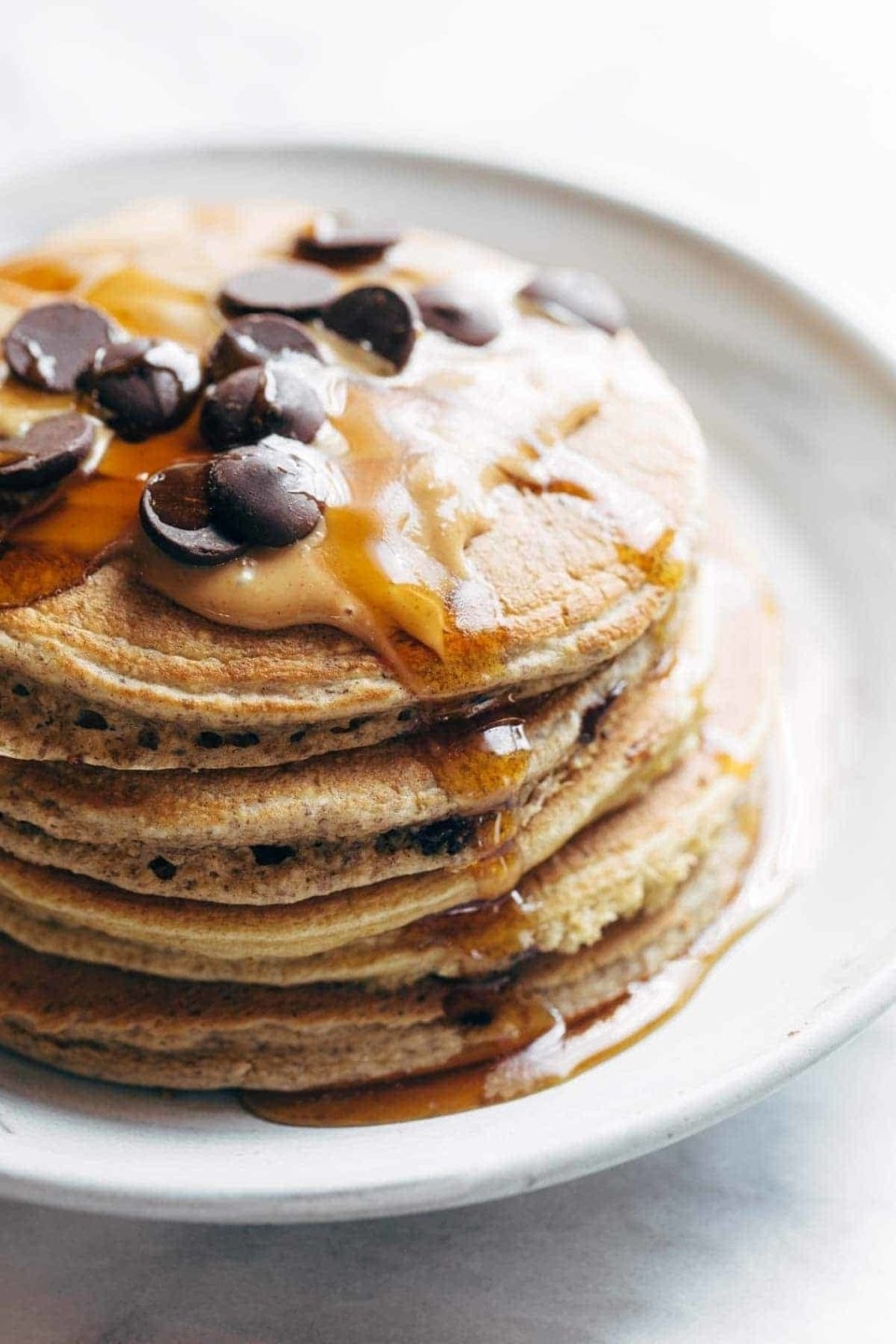 Stack of pancakes topped with chocolate chips and drizzled with syrup on a white plate